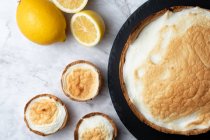 Вид на аппетитный пирог с безе, подаваемый на мраморном столе со свежими лимонами на кухне — стоковое фото