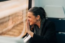 Вид сбоку позитивной женщины, размахивающей рукой и выглядывающей в окно, сидя на пассажирском сиденье во время поездки — стоковое фото