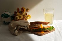 Sanduíche caseiro apetitoso com ovos escalfados e tomates frescos e alface servida com um copo de suco para o café da manhã na mesa com flores — Fotografia de Stock