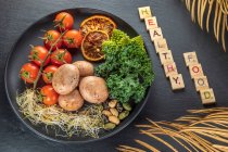 De arriba del título decorativo cerca de las patatas cocidas con el manojo de los tomates cherry y los retoños en el plato sobre el fondo gris - foto de stock