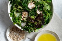Вид сверху свежего здорового салата в миске, подаваемого на стол с оливковым маслом и семенами подсолнечника — стоковое фото