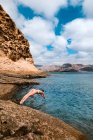 Full body of female traveler in swimwear jumping into rippling water of sea surrounded by rocky formations — Stock Photo