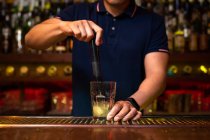 Неузнаваемый бармен, раздавливающий лимонные клинья в стакане во время приготовления коктейля мохито в баре — стоковое фото