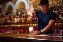 Молодий азіатський бармен виливає ром у скло, готуючи коктейль мохіто в барі. — стокове фото