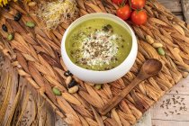 Draufsicht auf appetitliche vegane Sahnesuppe mit zerdrückten Pistazien auf Weidenmatte mit Holzlöffel — Stockfoto