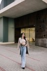 Empresária na moda em roupas elegantes andando na cidade e falando no telefone celular enquanto olha para longe — Fotografia de Stock