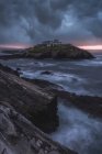 Paysage à couper le souffle de l'île rocheuse avec phare situé dans l'océan près de la côte rocheuse à Faro Tapia de Casariego dans les Asturies en Espagne sous un ciel nuageux au lever du soleil — Photo de stock