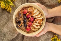 Anonyme Köchin zeigt Schüssel mit Bananenscheiben und verschiedenen frischen Beeren mit Karamellsoße zum Frühstück — Stockfoto