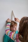 Sister helping brother with measuring him height with ruler and pencil near wall — Stock Photo