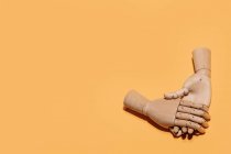Top view of wooden hands demonstrating handshake as sign of agreement placed on yellow background — Stock Photo