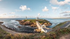 Spectaculaire paysage de pont menant à une île rocheuse couverte d'herbe verte avec phare placé dans l'océan ondulé à Faro Illa Pancha en Galice en Espagne pendant la journée — Photo de stock