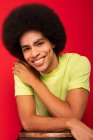 Joven auto alegre afroamericano masculino en camiseta casual mirando a la cámara en el fondo rojo - foto de stock