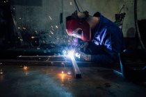 Trabalhador sem rosto nas luvas e detalhes de metal de soldagem uniforme na mesa perto de construções na fábrica — Fotografia de Stock