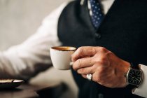 Crop of anonymous ethnic male entrepreneur in formal wear and wristwatch enjoy hot beverage from cup in coffee shop — Photo de stock
