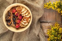 Overhead view of bowl with mix of ripe berries and banana slices covered with delicious caramel sauce on crumpled sackcloth — Stock Photo