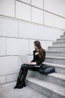 Vista lateral de una empresaria enfocada sentada en escalones de piedra en la ciudad y navegando por netbook mientras trabaja en el proyecto en línea - foto de stock