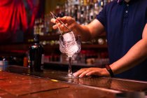 Barista irriconoscibile che mette un grande cubetto di ghiaccio nel bicchiere mentre prepara un cocktail tonico al gin nel bar — Foto stock