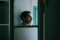 Calme homme torse nu avec barbe appuyée sur un mur minable à la maison et regardant loin — Photo de stock