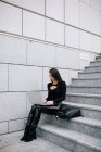 Seitenansicht einer fokussierten Unternehmerin, die auf Steintreppen in der Stadt sitzt und Netbook blättert, während sie an einem Online-Projekt arbeitet — Stockfoto