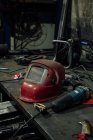 Mesa de metal com máscara de solda e moedor de ângulo perto de faca de papelaria e bobina com fio elétrico na garagem profissional — Fotografia de Stock