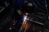 Trabalhador sem rosto nas luvas e detalhes de metal de soldagem uniforme na mesa perto de construções na fábrica — Fotografia de Stock