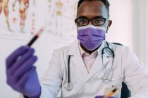 Médico varón afroamericano en guante médico demostrando probeta con muestra de sangre sobre fondo blanco - foto de stock