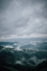 Живописный вид величественных гор с зелеными лесами под облачным небом в туманную погоду — стоковое фото