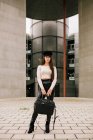 Junge trendige Unternehmerin steht am Eingang eines modernen Gebäudes in der Stadt und blickt in die Kamera — Stockfoto