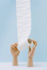 Zusammensetzung hölzerner Hände, die weiße Toilettenpapierrolle vor blauem Hintergrund abwickeln — Stockfoto