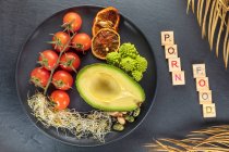 Vista dall'alto dell'iscrizione decorativa vicino al piatto con metà fresca di avocado e fascio di pomodorini vicino alle fette di arancia rossa — Foto stock