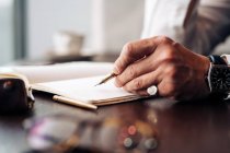 Schnupfen anonymer Geschäftsmann in Armbanduhr mit Stift und offenem Journal arbeiten am Cafeteria-Tisch bei Tageslicht — Stockfoto