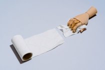 Composição de mãos de madeira desenrolamento rolo de papel higiênico branco contra fundo azul — Fotografia de Stock