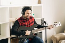 Stativ mit Kamera neben Mann beim Gitarrespielen im Hauszimmer platziert — Stockfoto