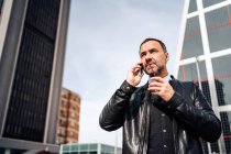 Mature Hispanic male executive in smart casual wear talking on cellphone while walk through the city — Stock Photo