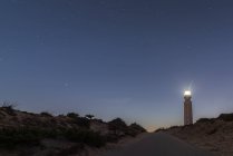 Lighthouse with bright lights placed on sandy beach in Faro de Trafalgar in Cadiz in Spain under night sky with stars — Stock Photo