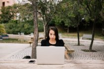 Focused female entrepreneur sitting at table with laptop in park working remotely — Stock Photo