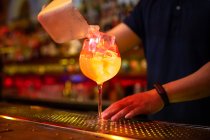 Руки невпізнаваного бармена, який кладе кубики льоду в склянку, готуючи грейпфрут і джинсовий коктейль у барі — стокове фото