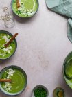 Vista superior de la deliciosa sopa de crema de guisantes en cuencos servidos en la mesa con servilleta y jarrón con flores - foto de stock
