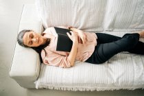 From above of sleepy middle aged female lying on comfortable sofa with plaid while resting in living room at home — Stock Photo