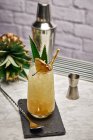 Yellow cocktail in glass garnished with pineapple piece and green leaves with paper straw placed on slate coaster with bar spoon — Stock Photo