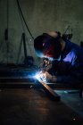 Lavoratore senza volto in guanti e dettagli metallici uniformi di saldatura sul tavolo vicino alle costruzioni in fabbrica — Foto stock