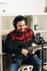 Stativ mit Kamera neben Mann beim Gitarrespielen im Hauszimmer platziert — Stockfoto