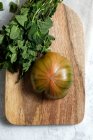 Dall'alto di pomodoro fresco rigato verde e rosso posto su tagliere in legno con mazzetto di fusti di menta — Foto stock