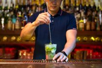 Неузнаваемый бармен, держащий стакан и мешающий коктейль мохито в баре — стоковое фото