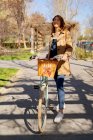 Полное тело веселой молодой женщины, улыбающейся и смотрящей в сторону старого велосипеда с плетеной корзиной — стоковое фото