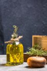Garrafa de vidro de óleo essencial com galhos de alecrim e vela de madeira orgânica em chamas na mesa cinza — Fotografia de Stock