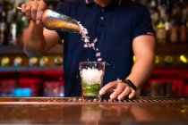 Unbekannter Barkeeper gießt Crushed Ice ins Glas, während er in der Bar einen Mojito-Cocktail zubereitet — Stockfoto