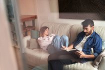 Tired young female in casual clothes sleeping on comfortable sofa near focused ethnic boyfriend reading book in daylight — Stock Photo