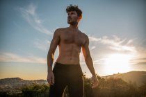 Shirtless male with six pack abs and beard looking away against mountains under cloudy sky in evening — Stock Photo