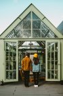Vista posteriore di una coppia di hipster alla moda in piedi su una terrazza in legno mentre si tengono per mano e si guardano le spalle — Foto stock